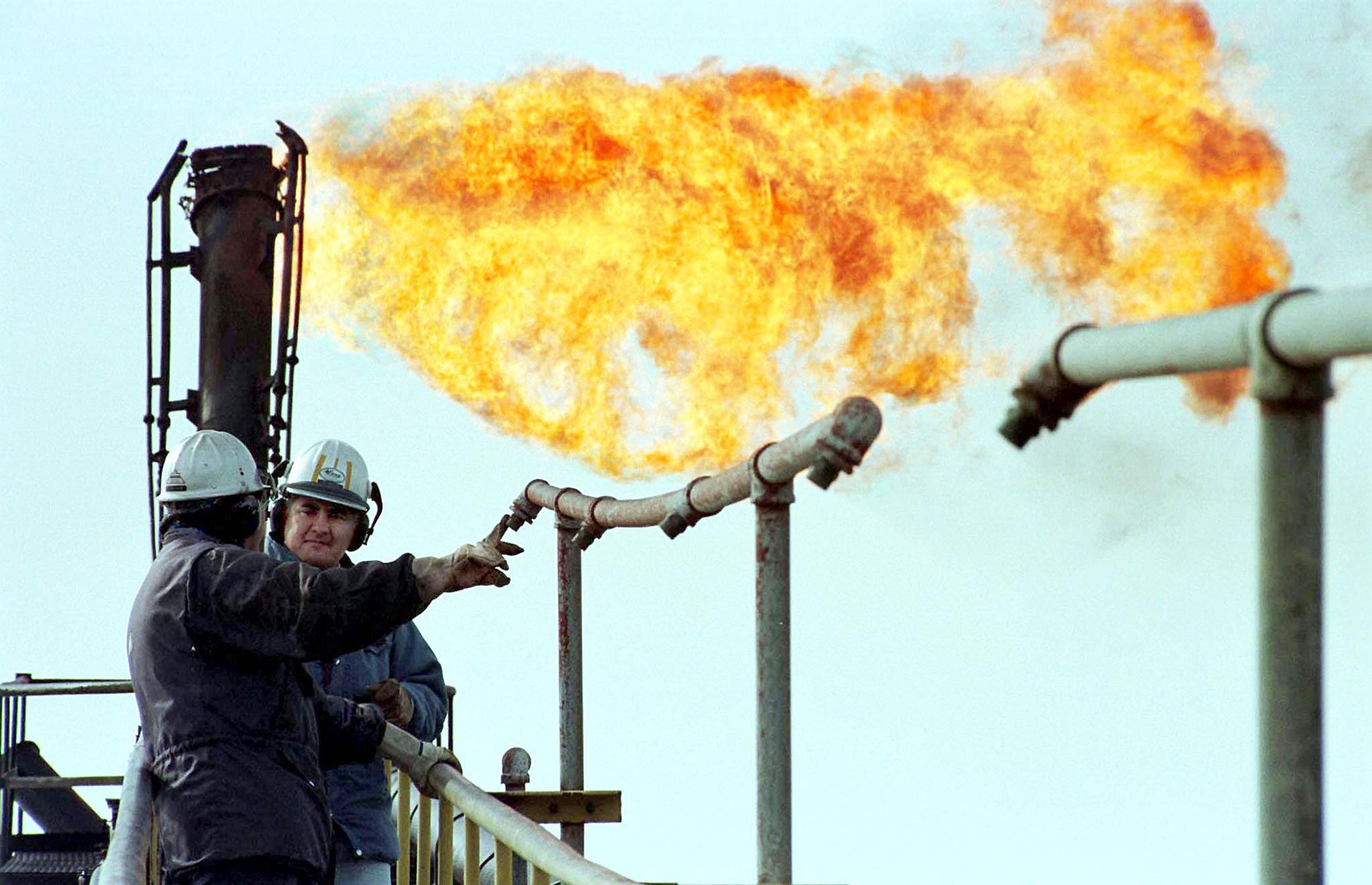 Petroleum industry workers confer on an offshore oil platform in Chile's Strait of Magellan while burning waste gas comes out of an exhaust pipe.